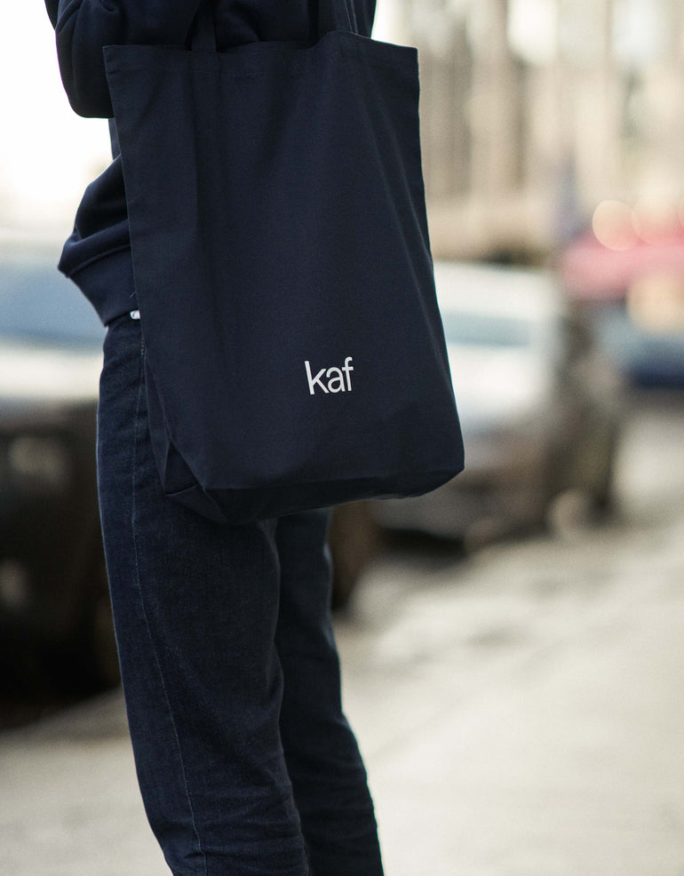 person wearing all navy wearing kaf branded tote bag.